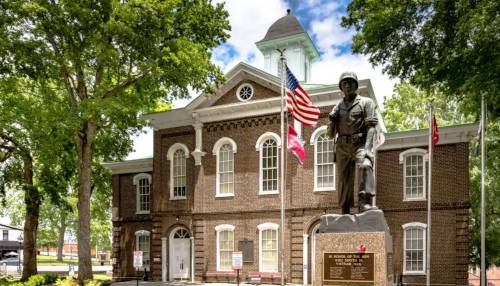 Loudon-Historic Historic brick courthouse in Loudon, Tennessee, with a soldier statue and American flag in front, surrounded by large trees.