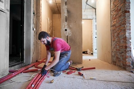 Young bearded plumber installing underfloor heating system in new apartment