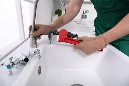 Professional plumber fixing water tap in kitchen closeup