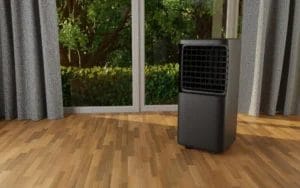 Portable black air conditioner unit on a wooden floor inside a room with large windows and curtains