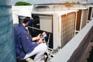 HVAC technician in safety gear checking rooftop air conditioning units with pressure gauges